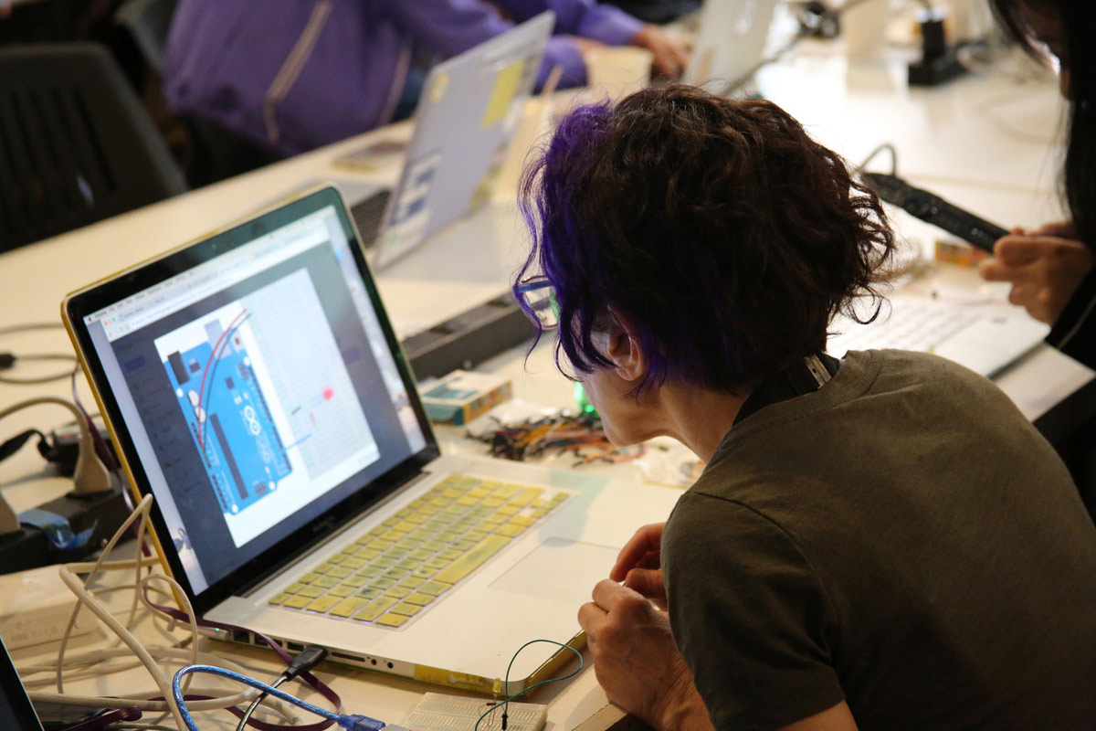 a woman referring to her laptop screen with an image of an Arduino